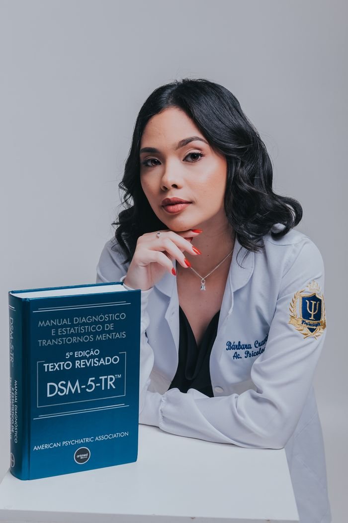 Female psychiatrist in white coat with DSM-5 manual, posing confidently.