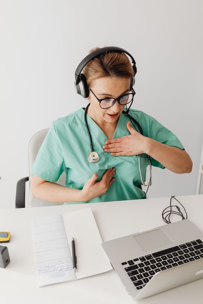 A female doctor in scrubs wearing headphones conducts an online consultation.