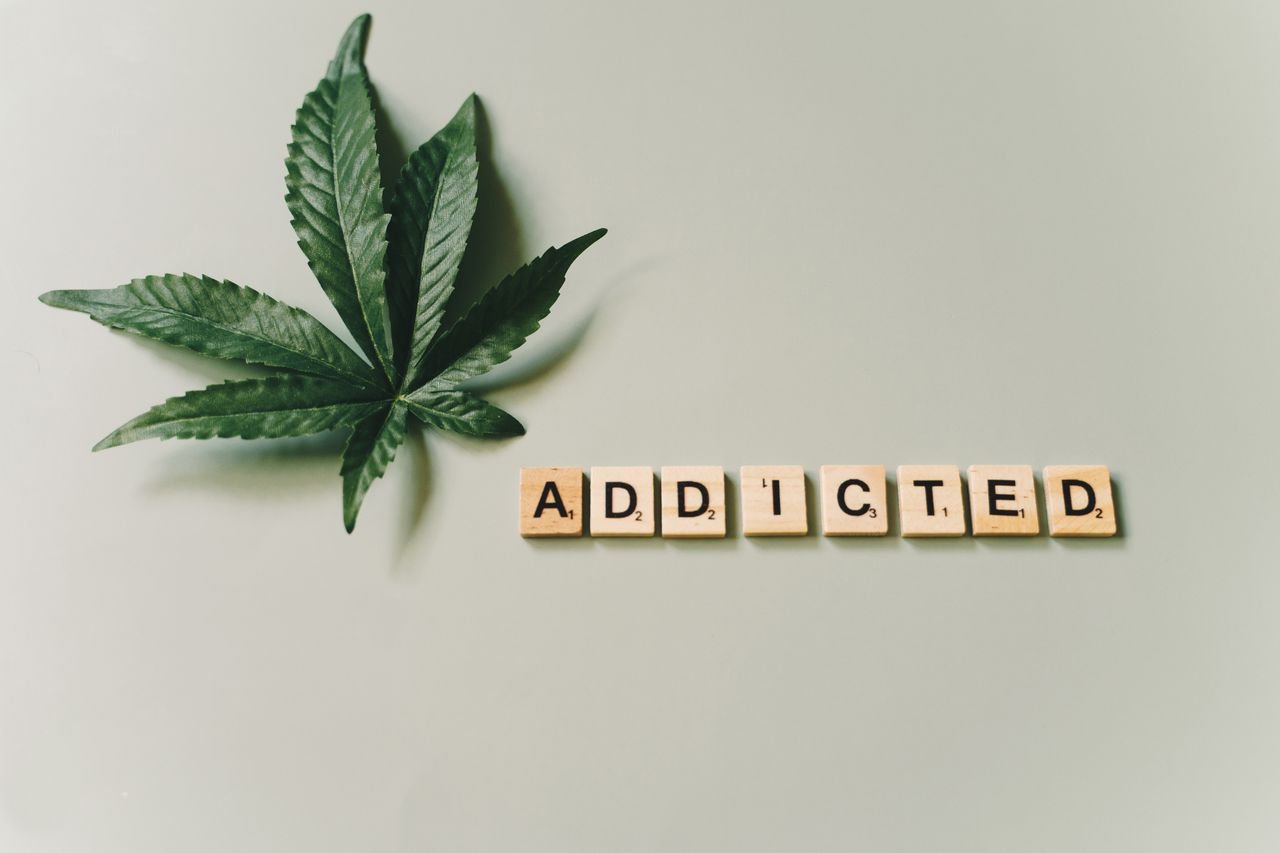 A cannabis leaf and wooden letter tiles spelling 'addicted' on a green surface.